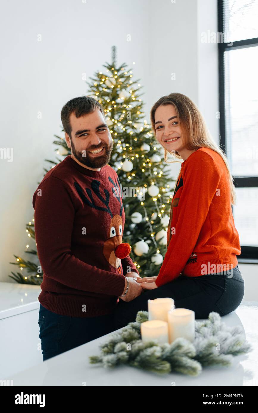 Attraktiver, fröhlicher Mann und Frau, die neben dem Weihnachtsbaum sitzen. Stockfoto