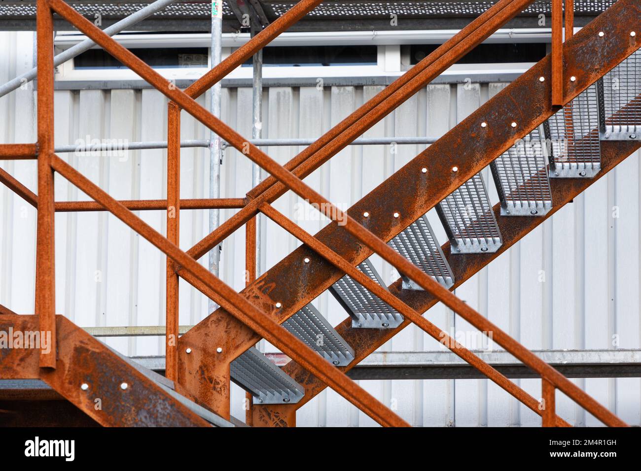 Eine Treppe mit rostigem Geländer verläuft an der Außenseite der hellen Wand einer Industriehalle entlang. Stockfoto