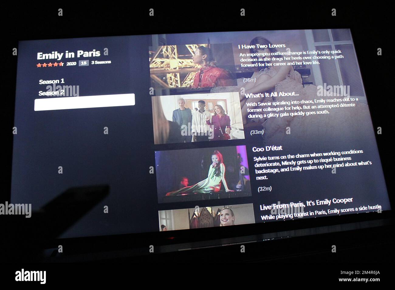 Die Netflix App auf dem fernsehbildschirm zeigt die Episoden der 3. Staffel der erfolgreichen Netflix TV-Show Emily in Paris mit dem Schatten einer Fernbedienung Stockfoto