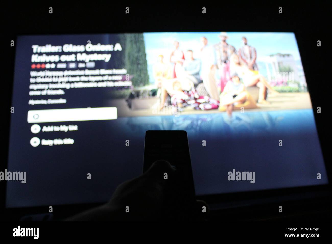 Ein Schatten der Hand hält die Fernbedienung vor dem verschwommenen fernsehbildschirm und sieht sich Netflix an. Konzept für die Wiedergabe von Netflix auf dem Fernseher zu Hause Stockfoto