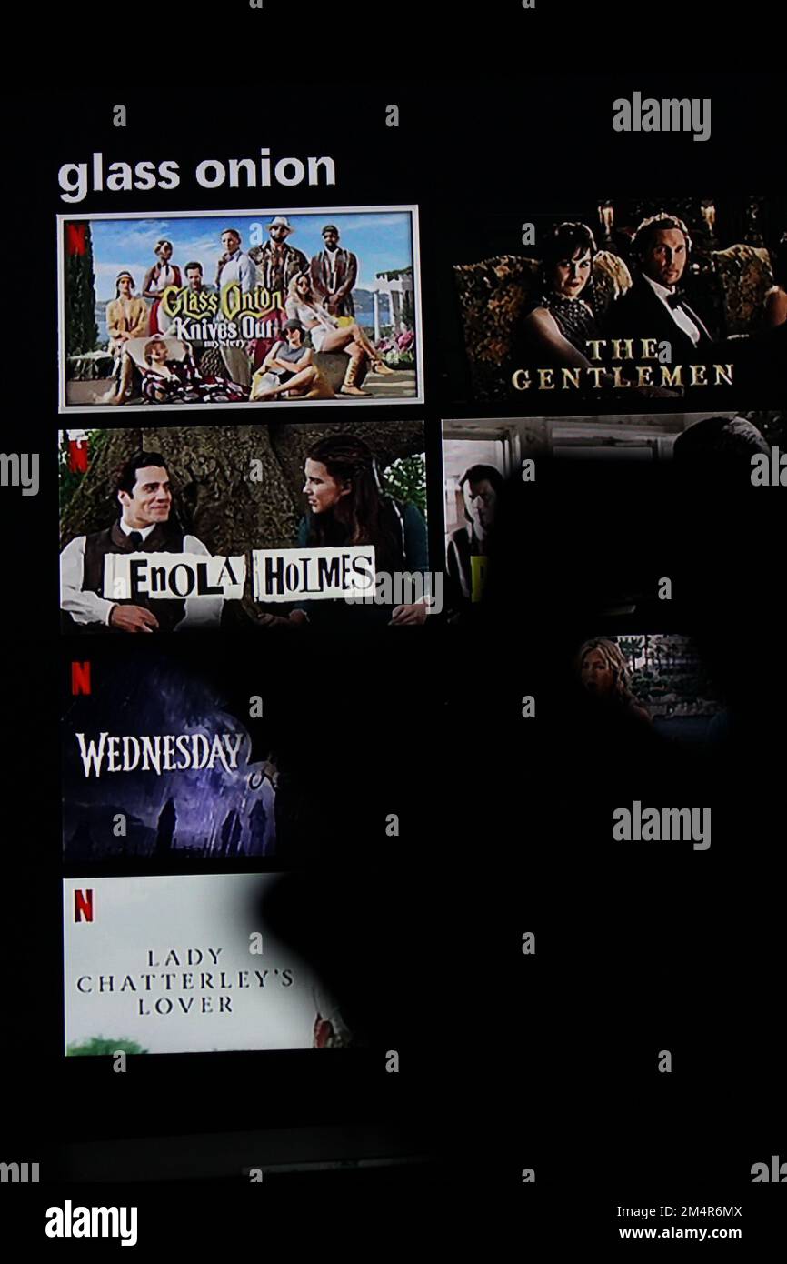 Netflix App auf einem fernsehbildschirm zeigt jemanden, der nach dem Netflix Film Glass Onion sucht, mit dem Schatten einer Fernbedienung vor sich. Konzeptblockbuster. Stockfoto