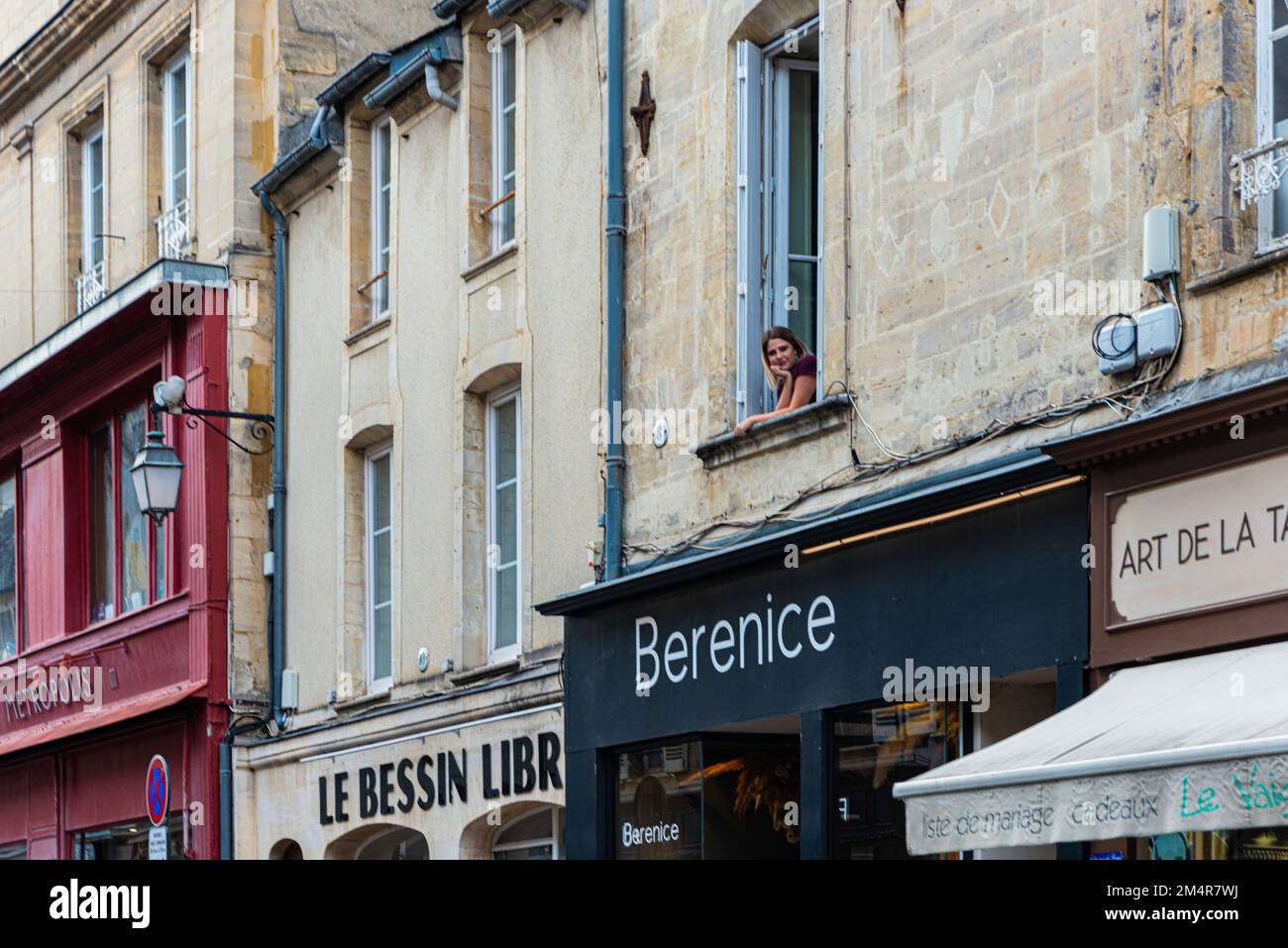 Eine Frau, die aus dem Fenster auf die Rue Saint Martin in der Innenstadt von Bayeaux, Frankreich schaut Stockfoto