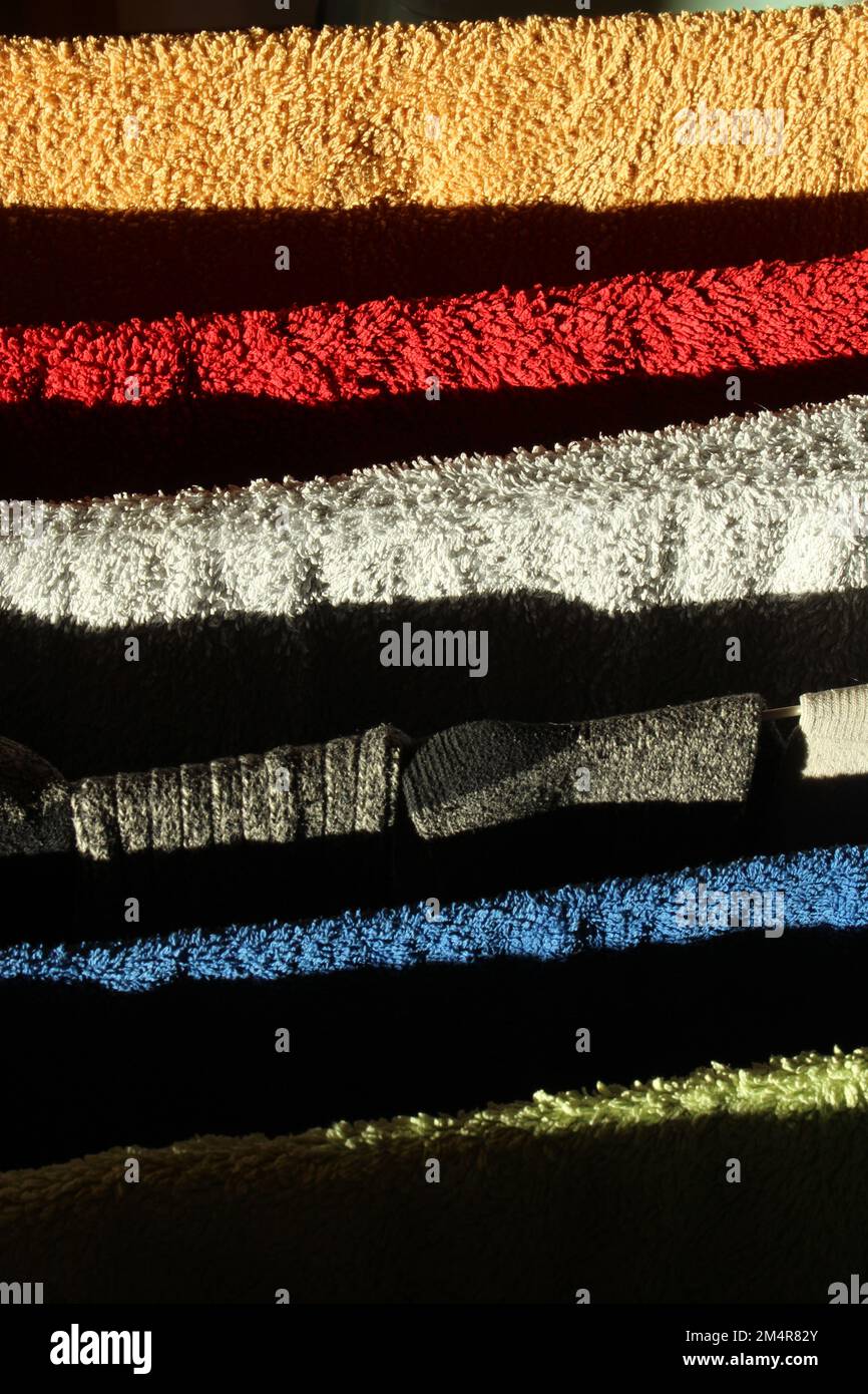 Einfache, helle Handtücher auf einem Wäschepferd, die mit natürlichem Licht trocknen und dramatische Schatten werfen. Abstrakter einheimischer Hintergrund mit kräftigen Farben und auffälligem Design Stockfoto