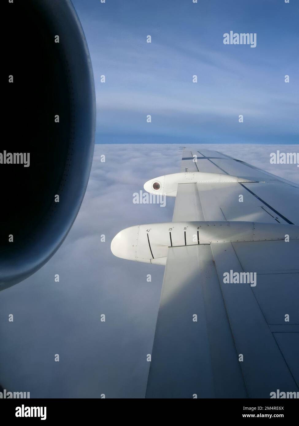 Blick aus dem Fenster auf den Flügel eines Düsenflugzeugs, das über den Wolken in 30,000 m Höhe fliegt. Der Motor befindet sich im Vordergrund Stockfoto