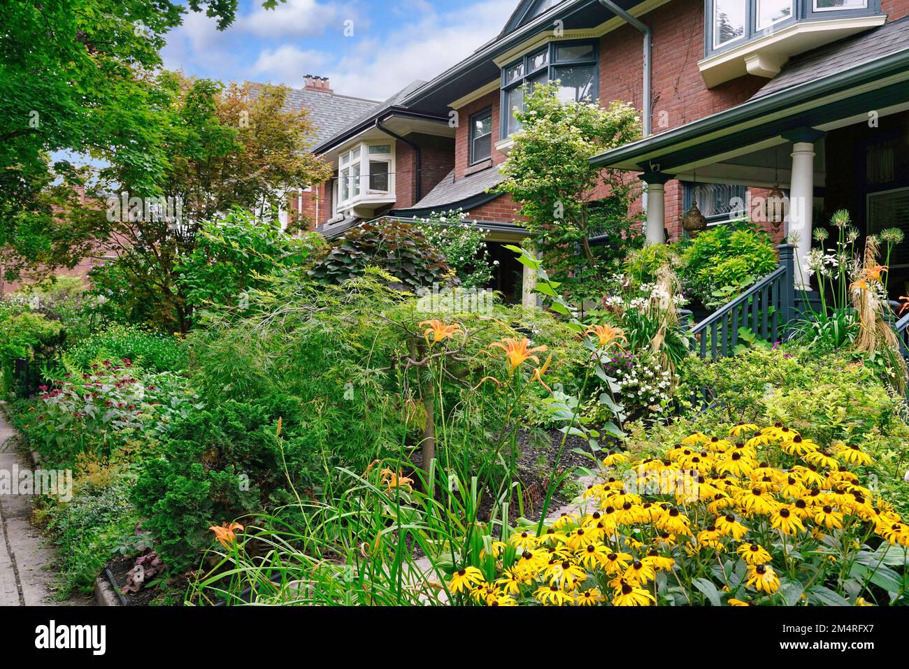 Wohnstraße mit älteren Häusern und Vorhöfen voller Blumen Stockfoto