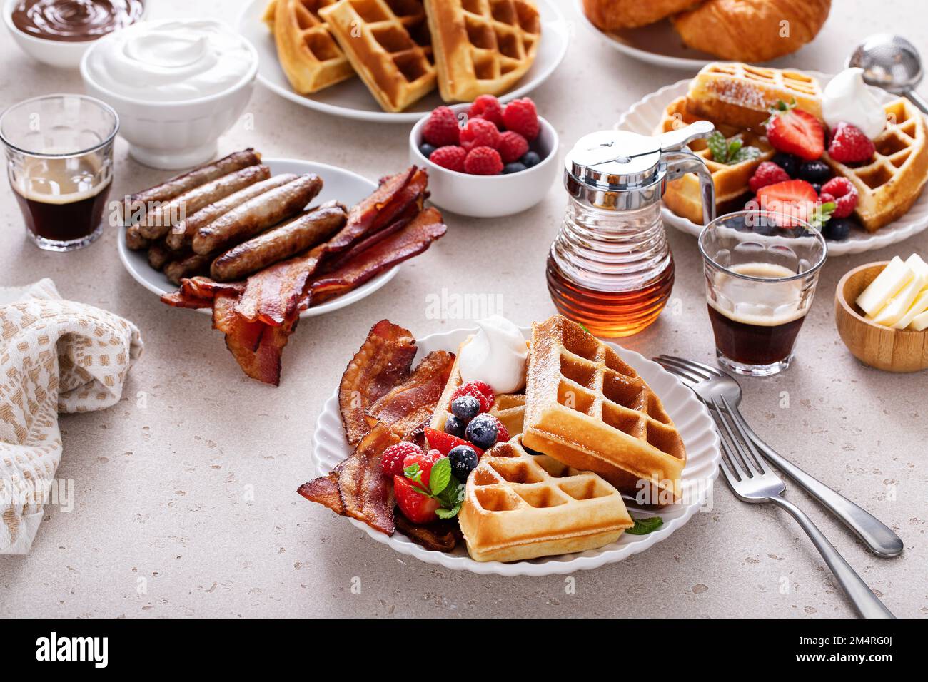 Frühstückstisch mit Waffeln, Croissants und Speck Stockfoto