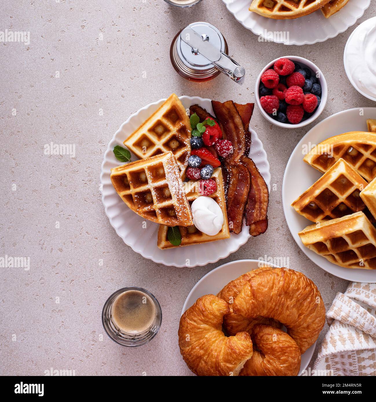 Frühstückstisch mit Waffeln, Croissants, Wurst und Speck serviert mit ...