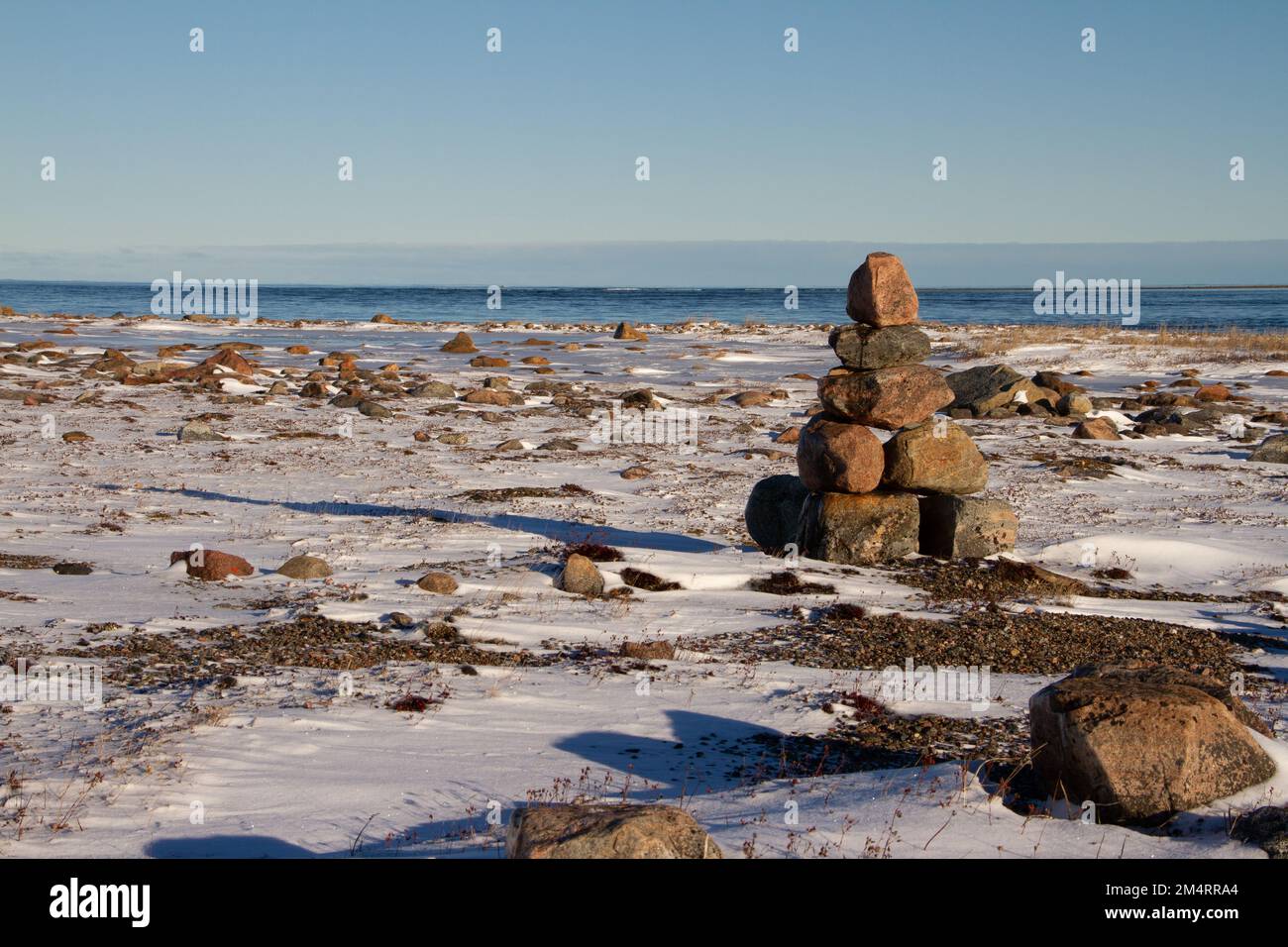 Arktische Landschaft - ein Wahrzeichen von Inuksuk oder Inukshuk auf einer schneebedeckten arktischen Tundra in Nunavut an einem klaren, sonnigen Tag in der Nähe von Arviat, Nunavut, Kanada Stockfoto