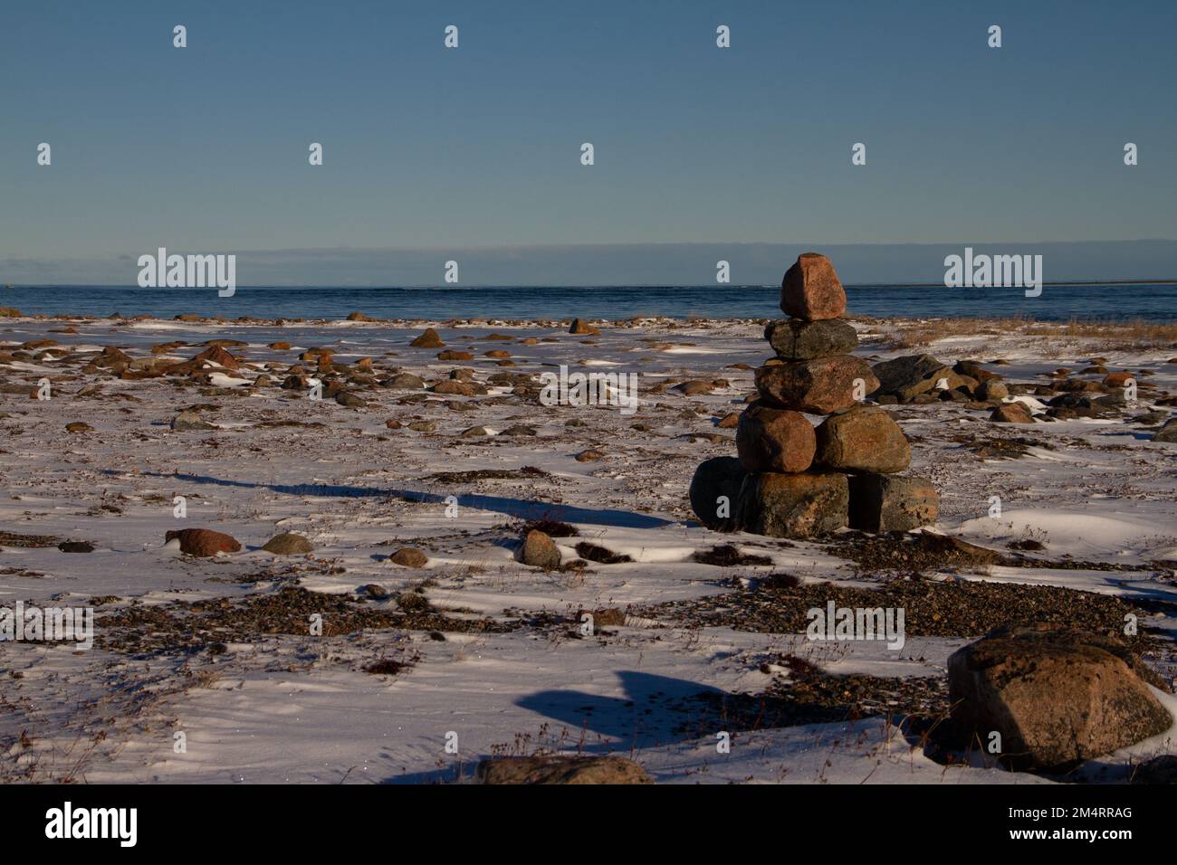 Arktische Landschaft - ein Wahrzeichen von Inuksuk oder Inukshuk auf einer schneebedeckten arktischen Tundra in Nunavut an einem klaren, sonnigen Tag in der Nähe von Arviat, Nunavut, Kanada Stockfoto