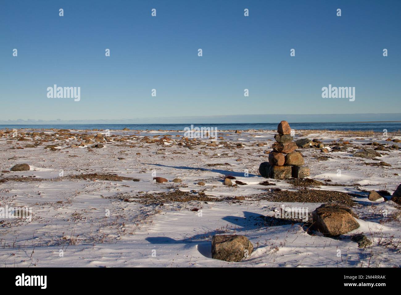 Arktische Landschaft - ein Wahrzeichen von Inuksuk oder Inukshuk auf einer schneebedeckten arktischen Tundra in Nunavut an einem klaren, sonnigen Tag in der Nähe von Arviat, Nunavut, Kanada Stockfoto