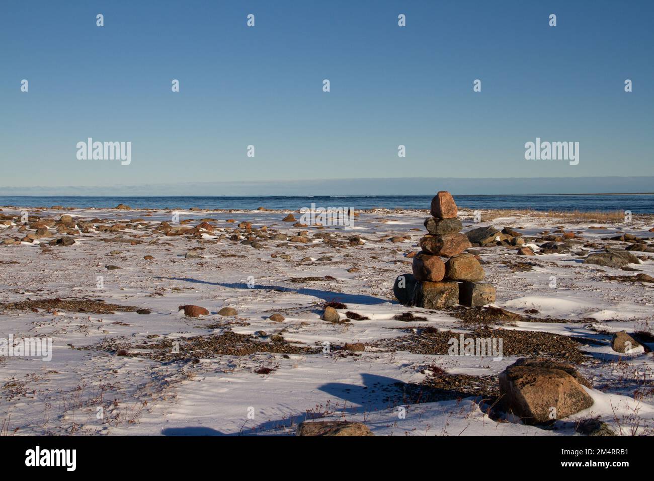 Arktische Landschaft - ein Wahrzeichen von Inuksuk oder Inukshuk auf einer schneebedeckten arktischen Tundra in Nunavut an einem klaren, sonnigen Tag in der Nähe von Arviat, Nunavut, Kanada Stockfoto