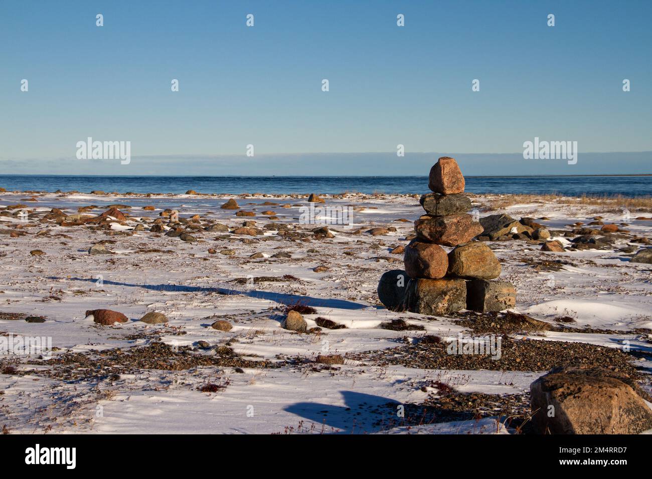 Arktische Landschaft - ein Wahrzeichen von Inuksuk oder Inukshuk auf einer schneebedeckten arktischen Tundra in Nunavut an einem klaren, sonnigen Tag in der Nähe von Arviat, Nunavut, Kanada Stockfoto