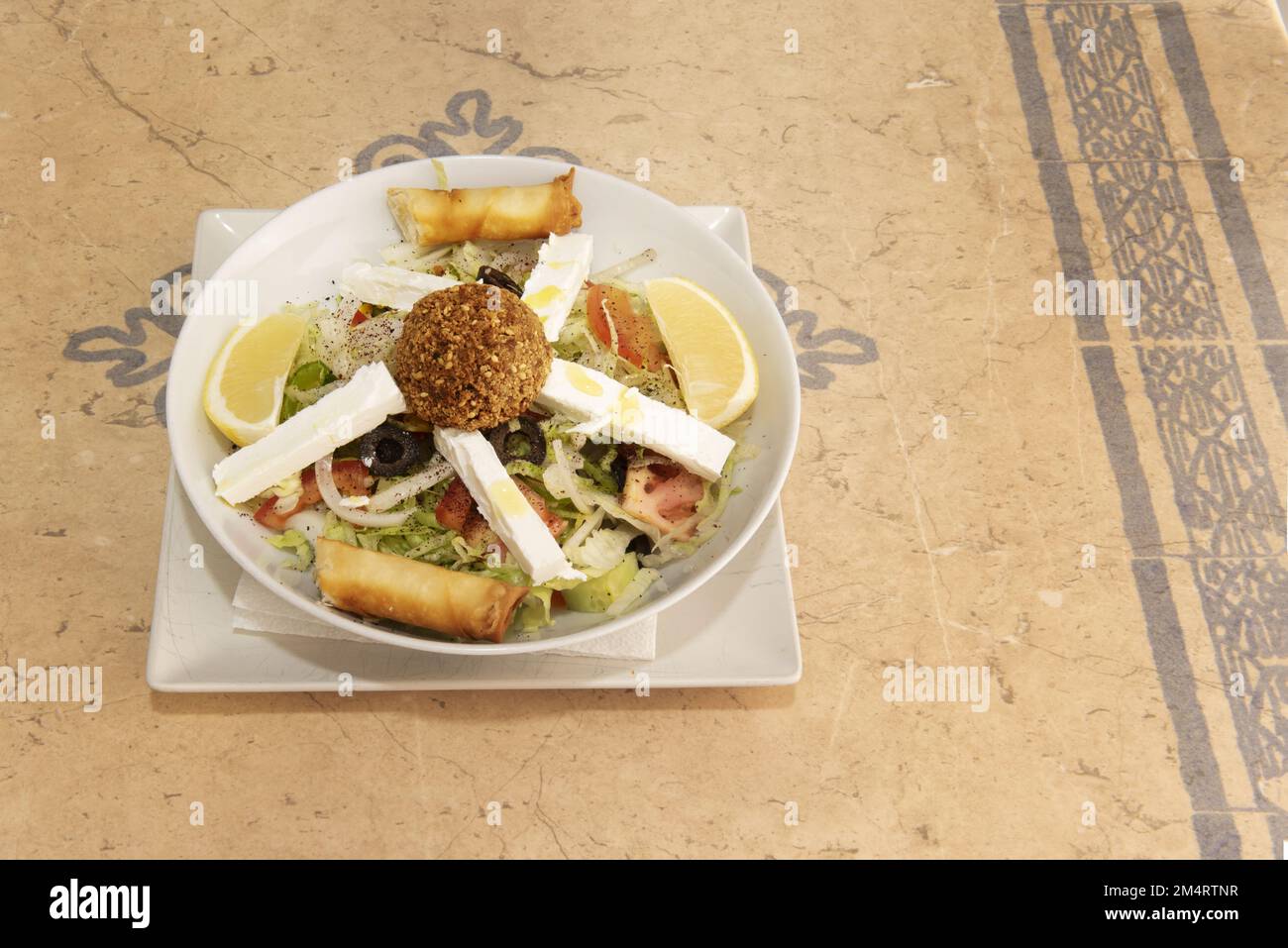 Ein marokkanischer Salat mit frischem Fetakäse, Pfeffer, schwarzen Oliven, Falafel-Kugel, weißen Zwiebeln und Eisbergsalat mit Zitronenschnitten Stockfoto