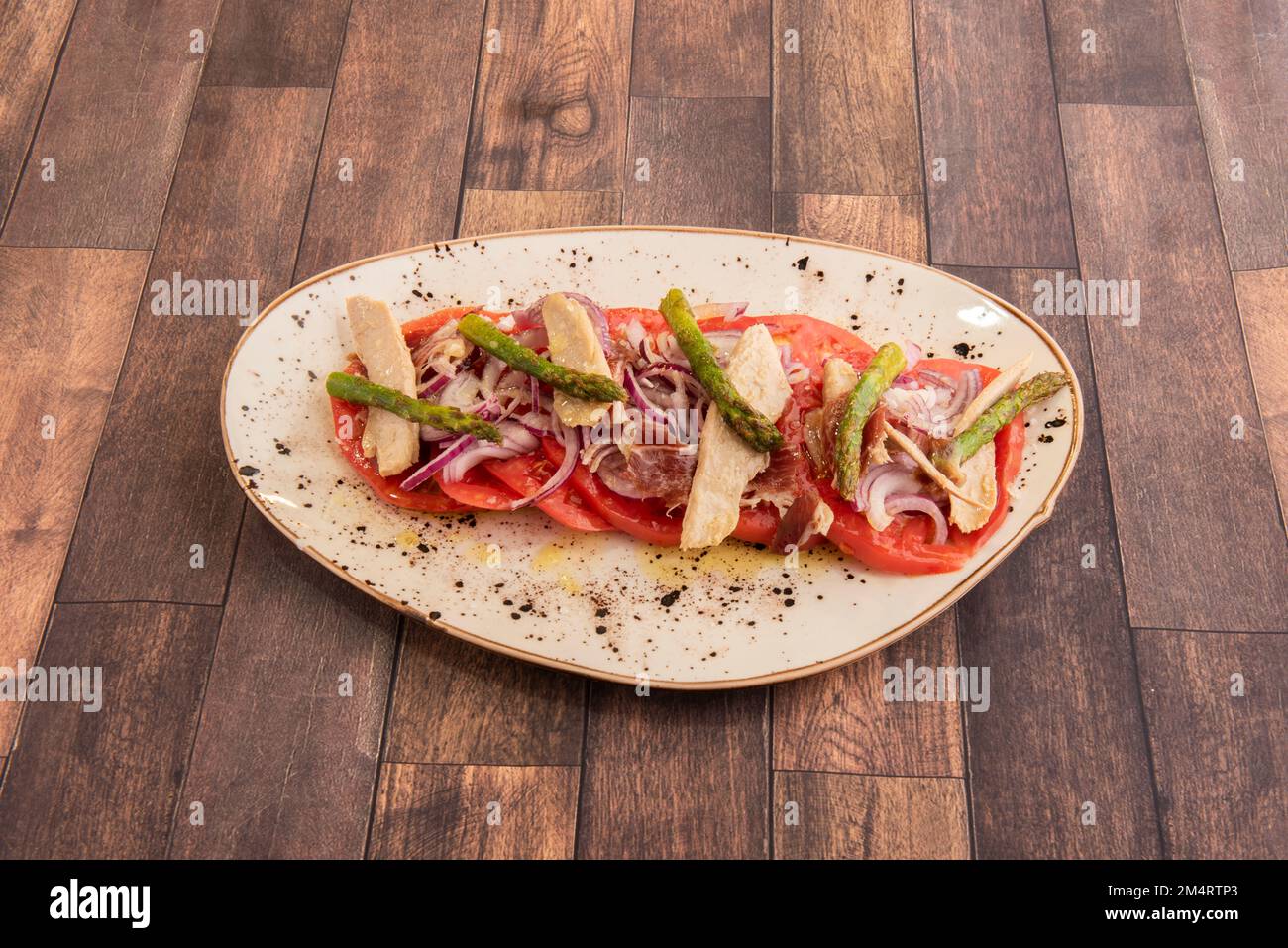 Ein traditioneller spanischer Thunfisch-Bauchsalat mit vielen roten Zwiebeln, Tomatenscheiben, viel Olivenöl und Salz und wildem Spargel Stockfoto