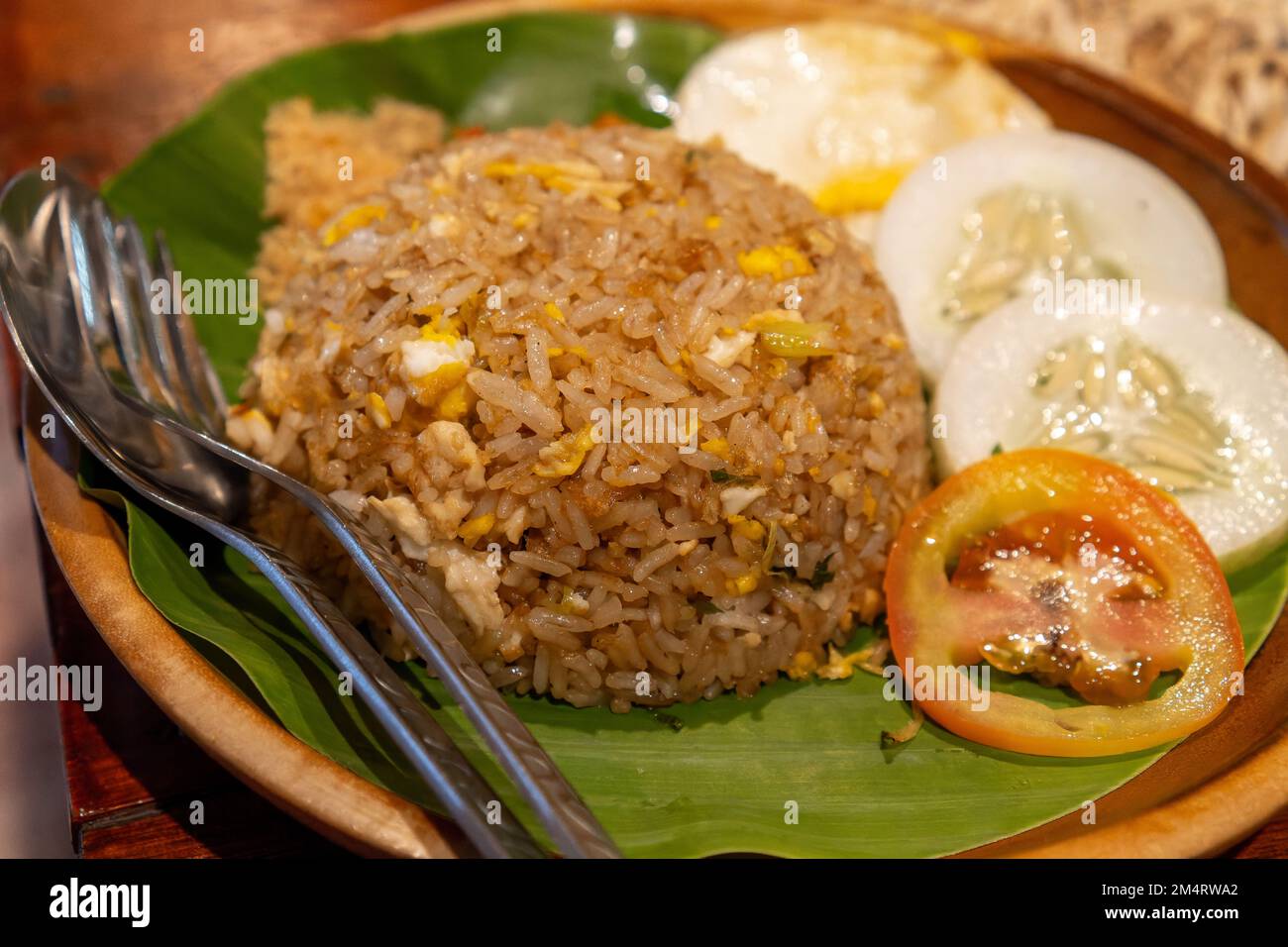 Gebratener Reis, gemischt mit Ei, Gurke und tomatoes-Scheiben. Serviert auf einem Holzteller mit Bananenblättern Stockfoto