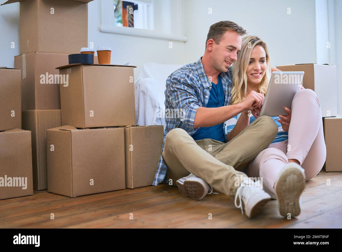 Sie haben jede Menge Ideen, um ihr neues Zuhause zu dekorieren. Ein junges Paar, das ein digitales Tablet benutzt, während es umzieht. Stockfoto