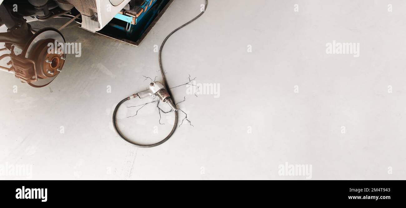 Druckluft-Schlagschrauber mit Gummischlauch auf dem Boden in der Autowerkstatt, Kopierraum Stockfoto