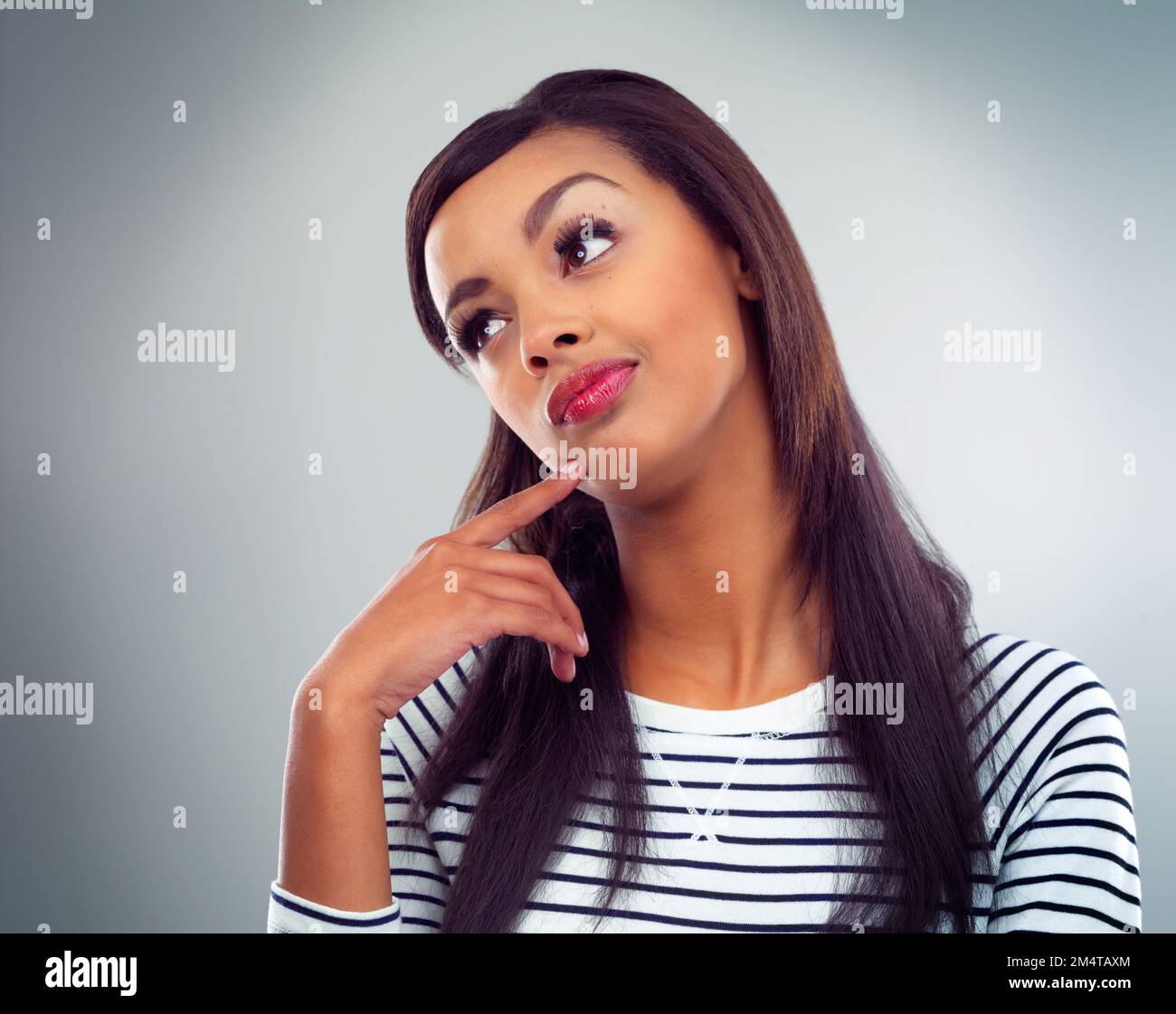Ich denke über ihre nächste Pose nach. Eine junge Frau, die vor grauem Hintergrund posiert. Stockfoto
