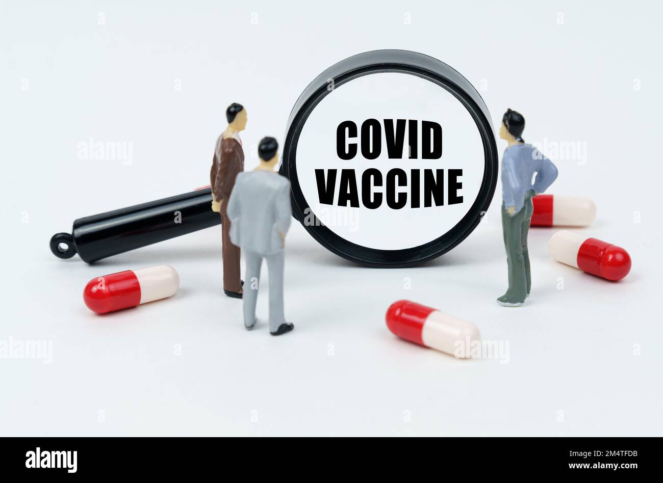 Medizinisches Konzept. Auf einer weißen Oberfläche sind Pillen, Miniaturfiguren von Menschen und eine Lupe mit der Inschrift - COVID-IMPFSTOFF Stockfoto