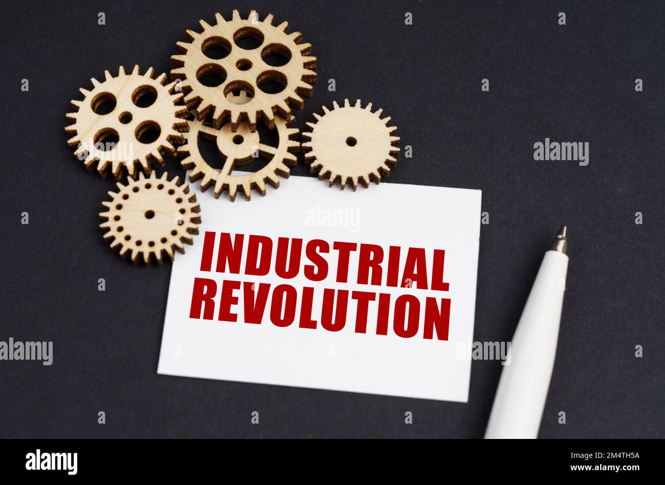 Industriekonzept. Auf der schwarzen Oberfläche befinden sich Zahnräder, ein Stift und eine Visitenkarte mit der Aufschrift "Industrielle Revolution" Stockfoto