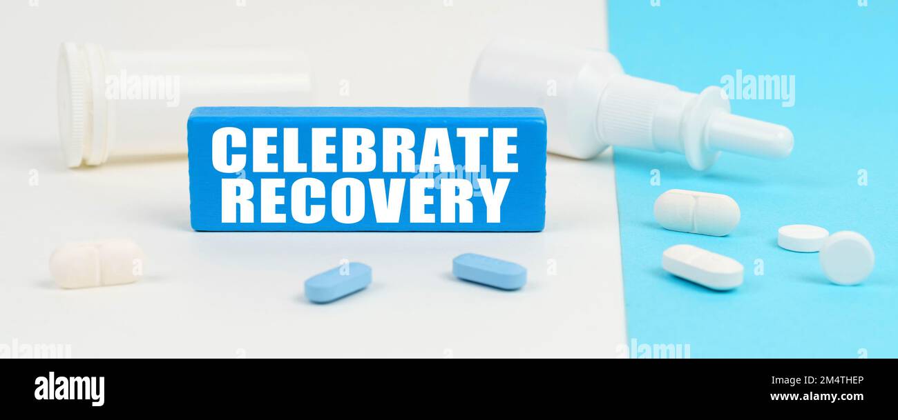 Medizinisches Konzept. Auf einer weißen und blauen Oberfläche sind Pillen, ein Spray und ein Holzschild mit der Inschrift - Celebrate Recovery Stockfoto