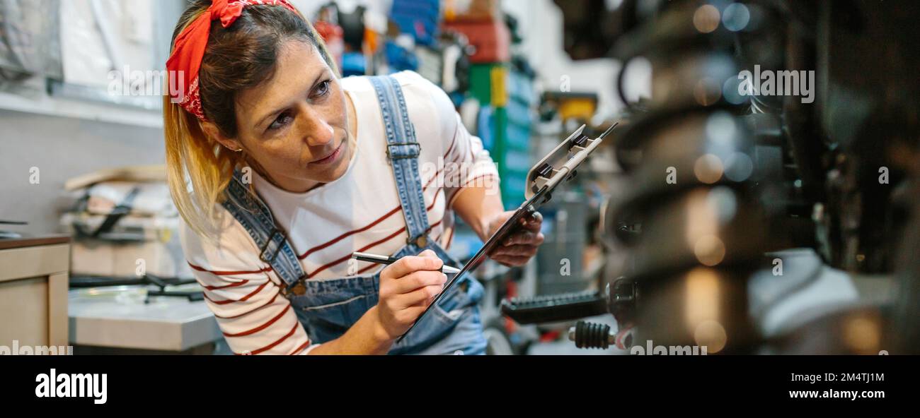 Eine Mechanikerin, die die Motorraddokumentation in der Garage ausfüllt Stockfoto