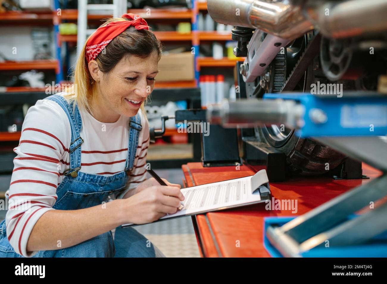 Eine Mechanikerin, die die Motorraddokumentation in der Garage ausfüllt Stockfoto