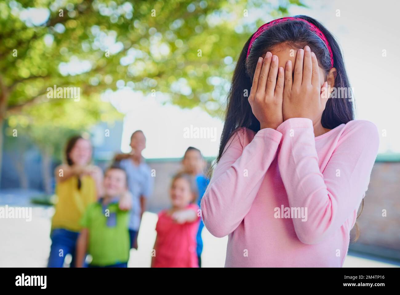 Ich wünschte, das Mobbing könnte aufhören. Ein junges Mädchen, das ihr Gesicht verdeckt, während sie draußen gemobbt wird. Stockfoto