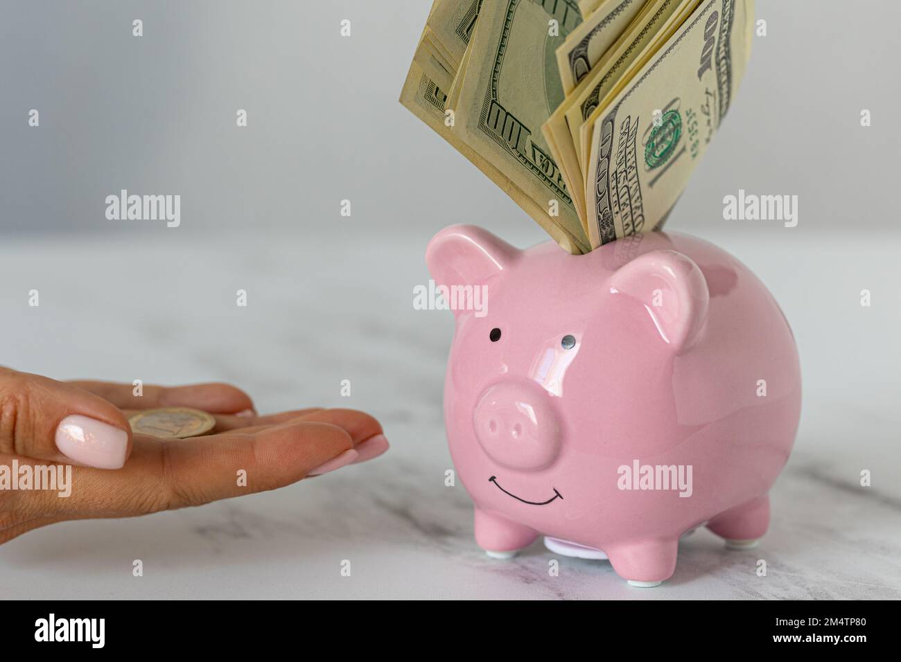 Nahaufnahme eines Sparschweines mit Dollars und einer Frau, die Euromünzen auf dem Bürotisch ausstreut. Wirtschaft, Krise und Inflation. Kostenmanagement Stockfoto