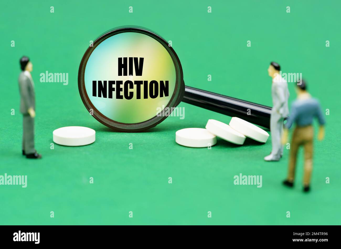 Medizinisches Konzept. Auf einer grünen Oberfläche sind Pillen, Miniaturfiguren von Menschen und eine Lupe mit der Inschrift - HIV-Infektion Stockfoto