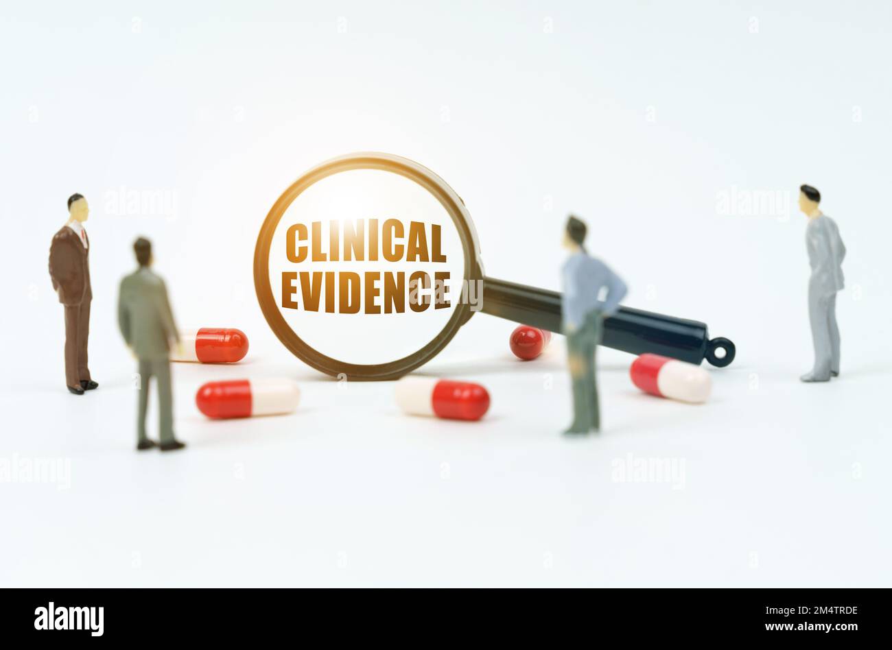 Medizinisches Konzept. Auf einer weißen Oberfläche sind Pillen, Figuren von Menschen und eine Lupe mit der Inschrift - Klinische Evidenz Stockfoto