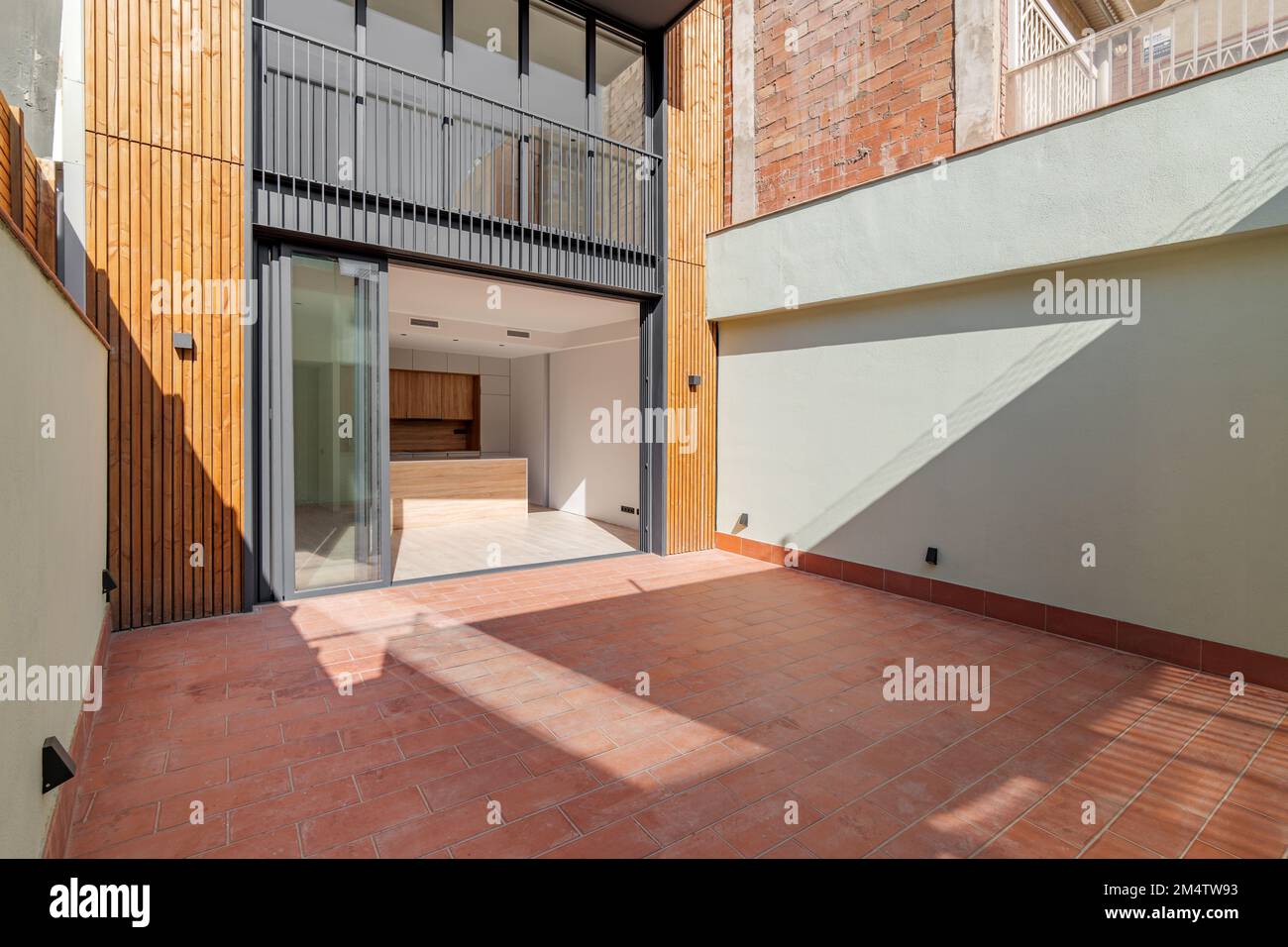 Mehrstöckiges Wohngebäude mit Schiebetüren aus schwarzem Metall und Glas. Die Tür führt zur Küche mit hellen Holzmöbeln. Terrasse Stockfoto