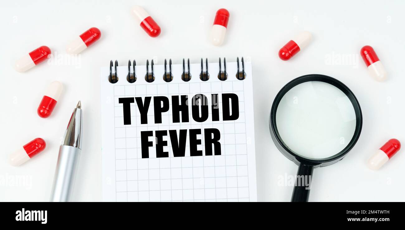 Medizinisches Konzept. Auf einer weißen Oberfläche befinden sich Tabletten, ein Stift, eine Lupe und ein Notizblock mit der Aufschrift - TYPHUS Stockfoto