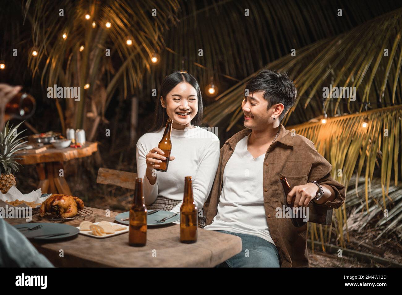 Ein junges asiatisches Paar, das auf einer Gartenparty mit Bier anstoßen will Stockfoto