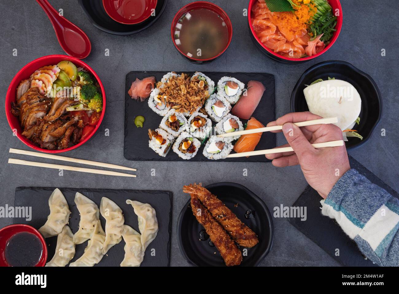 Sushi-Brötchen essen. Japanisches Speiserestaurant, verschiedene Sushi-Platten. Nahaufnahme der Hand mit gerollten Essstäbchen mit rustikalem Hintergrund. Stockfoto