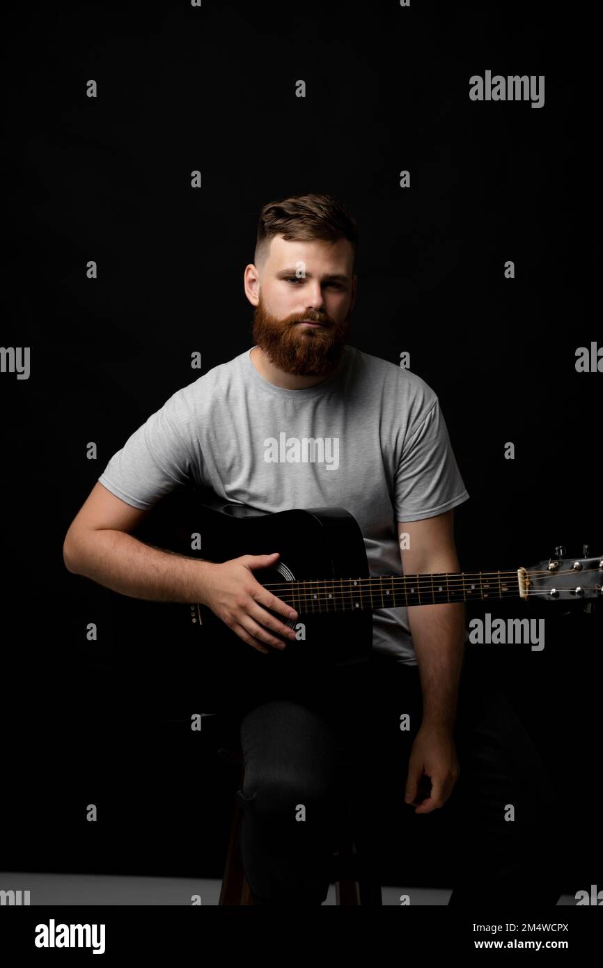 Ein bärtiger Musiker, der in einem dunklen Raum Akustikgitarre spielt. Stockfoto