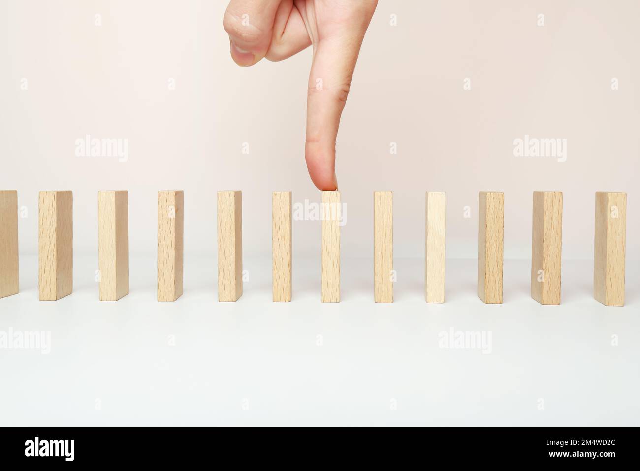 Dominosteine stehen in einer Reihe. Der Zeigefinger der Hand auf einem hölzernen Domino. Stockfoto