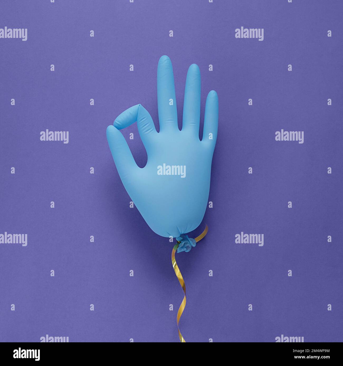 Medizinische Handschuhe aus blauem Latex als Ballon auf violettem Hintergrund, zeigt den Charakter in Ordnung. Farbig in sehr peripher - Farbe des Jahres 2022. Minimalismuskonzept. Stockfoto