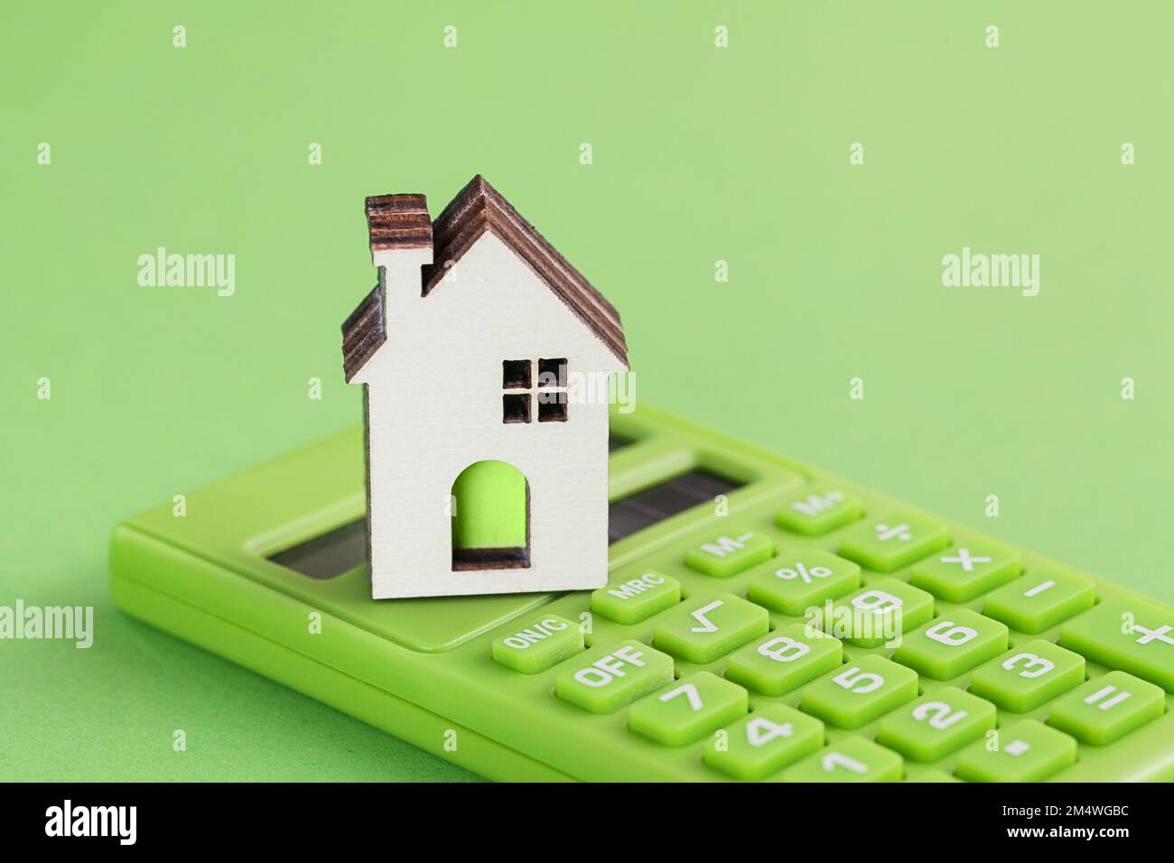 Weißes Haus, grüner Taschenrechner auf grünem Hintergrund. Eco-Konzept. Wohnungsbau und Versicherung. Stockfoto