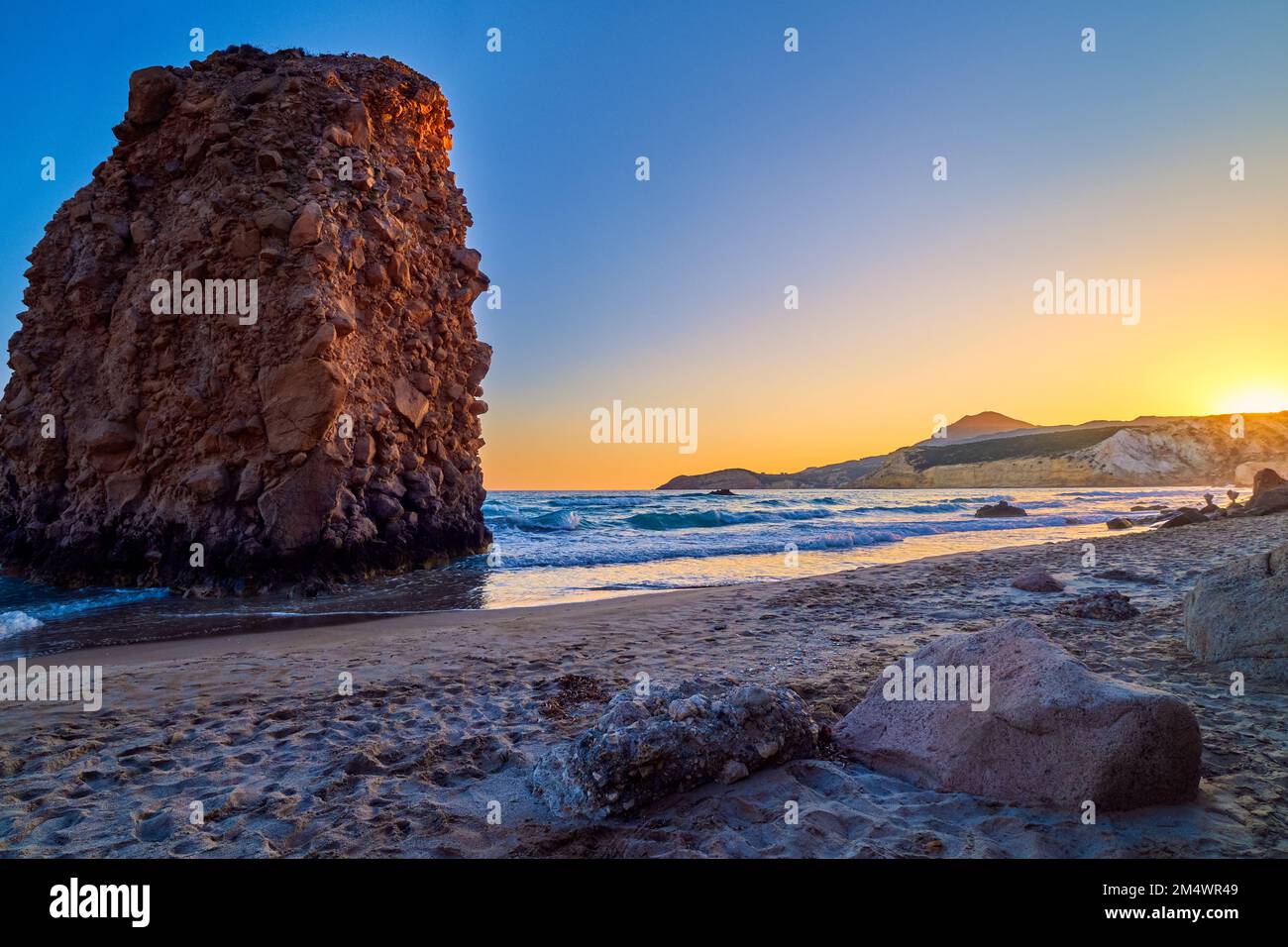 Farbenfroher Sonnenuntergang am Strand von Fyriplaka, Milos, Griechenland. Keine Menschen, niedrige Sonne. Ikonischer Fyriplaka einsamer Felsen gegen niedrige Sonne, farbenfrohen Himmel und Meer Stockfoto
