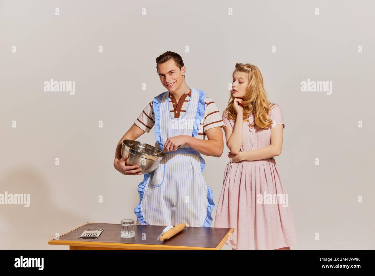 Das Aufbrechen von Geschlechterstereotypen. Freundliches Familienpaar in Retro-Kleidung kocht in der Küche isoliert vor hellem Hintergrund. Beziehungskonzept Stockfoto