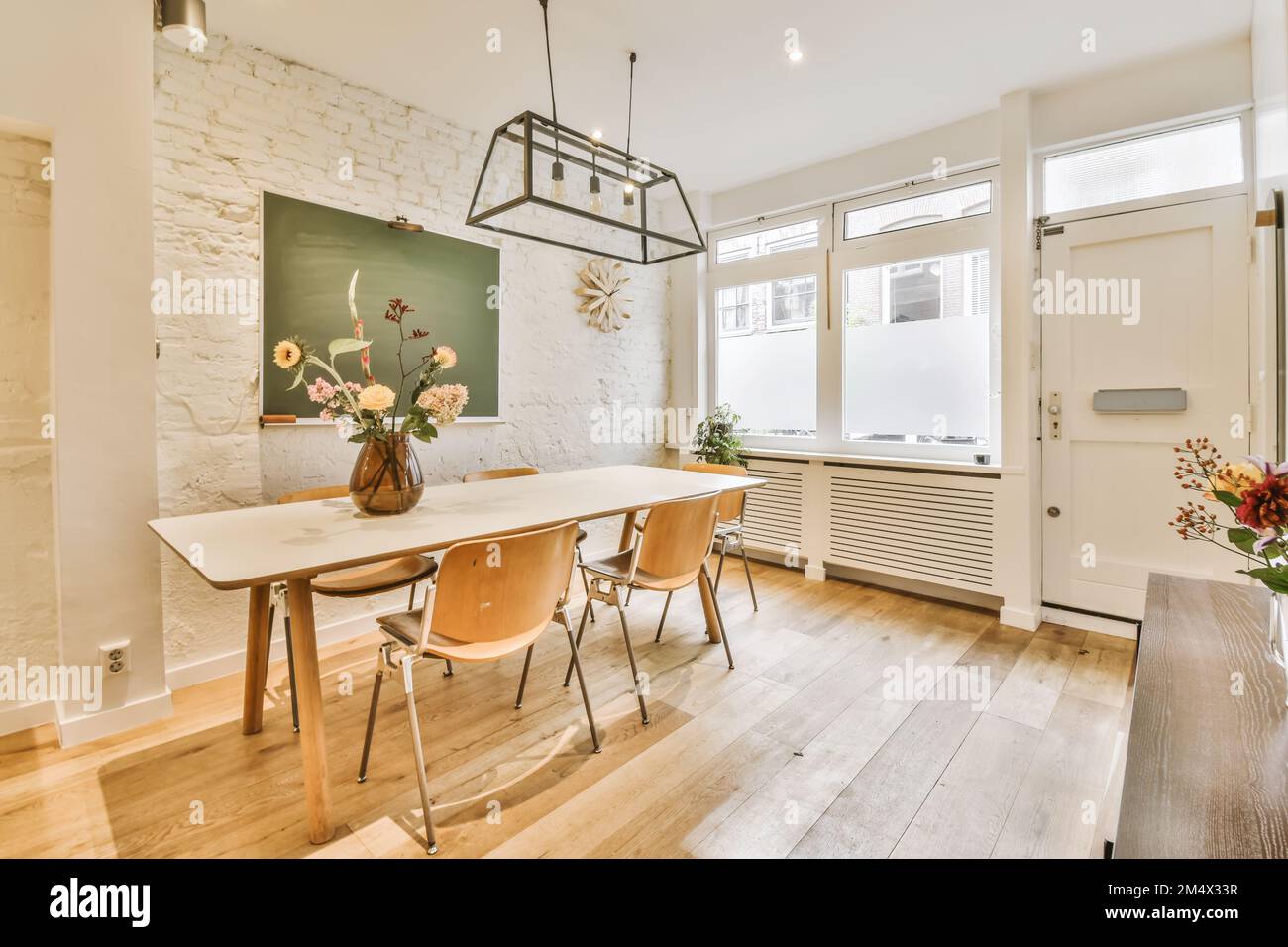 Ein Speisesaal mit weißen Backsteinwänden und Holzfußboden in der Mitte des Raums ist eine grüne Tafel an der Wand Stockfoto