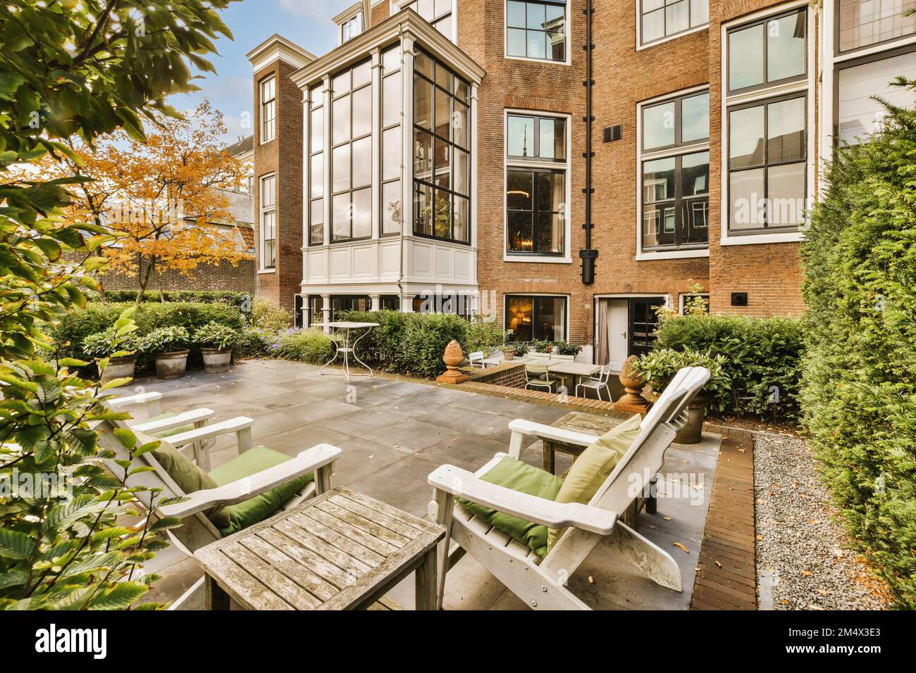 Ein Terrassenbereich mit Stühlen und Tischen im mittleren Teil eines Apartmentgebäudes, das von grünen Bäumen umgeben ist Stockfoto