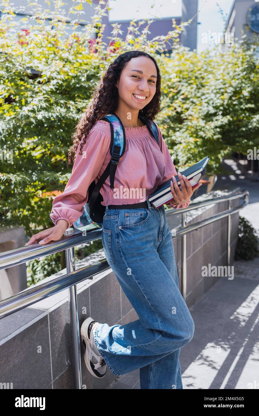 Eine glückliche, junge schwarze Studentin, die ihre Bücher auf dem Campus hält. Gesundes Selbstvertrauen Stockfoto