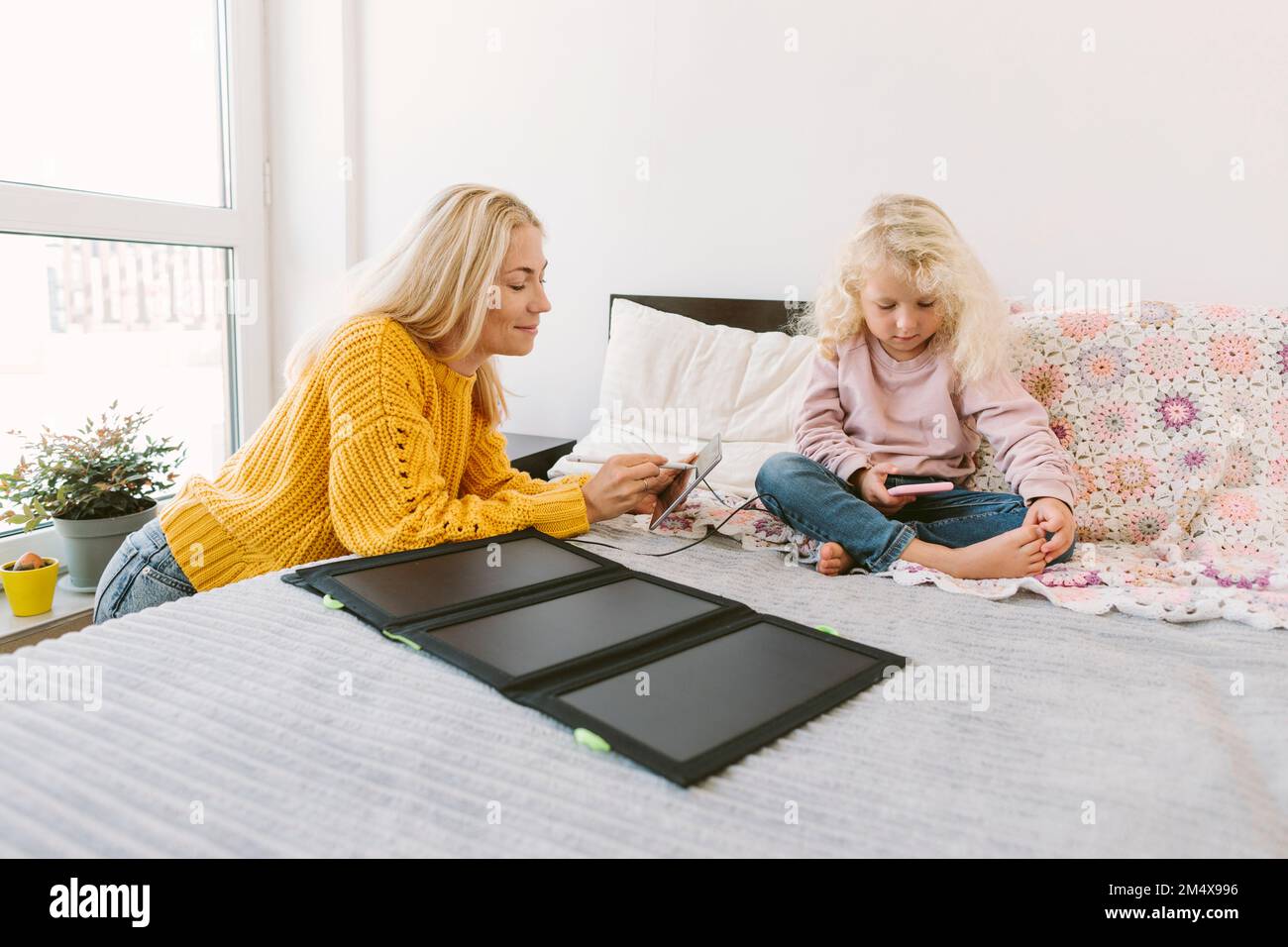 Lächelnde Mutter, die einen Tablet-PC mit Solar-Ladegerät auf dem Bett benutzt Stockfoto