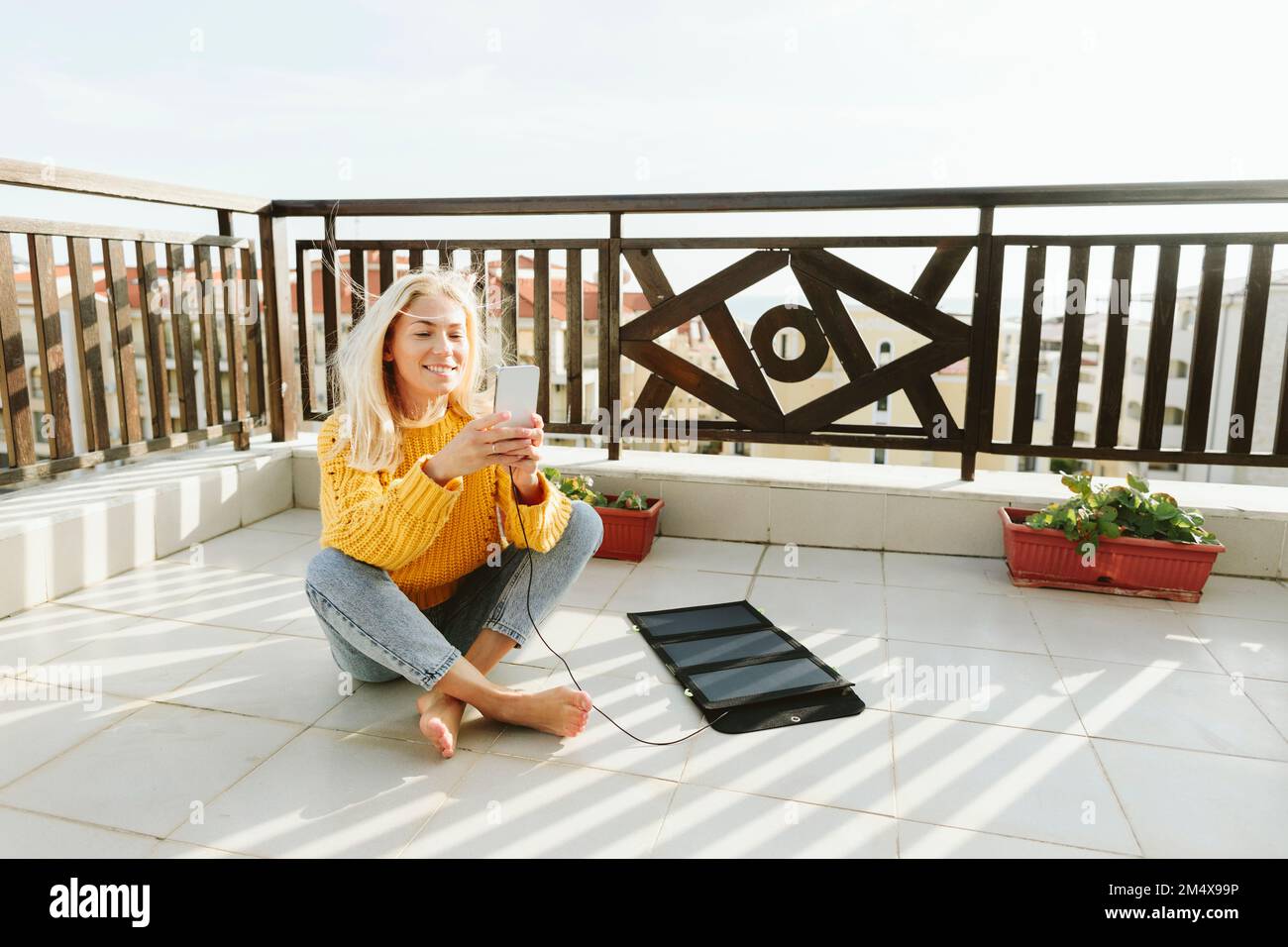 Lächelnde Mutter, die Mutter mit Solar-Ladegerät auf der Terrasse zu Hause benutzt Stockfoto