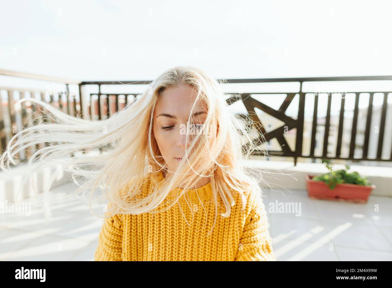 Blonde Frau mit windgepeitschtem Haar auf der Terrasse Stockfoto