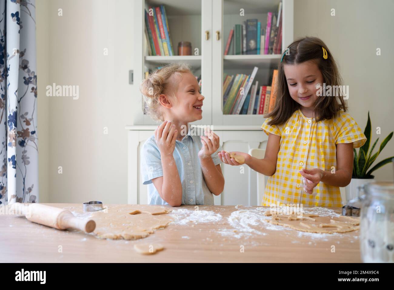 Fröhliche süße Mädchen, die zu Hause Kekse mit Teig zubereiten Stockfoto