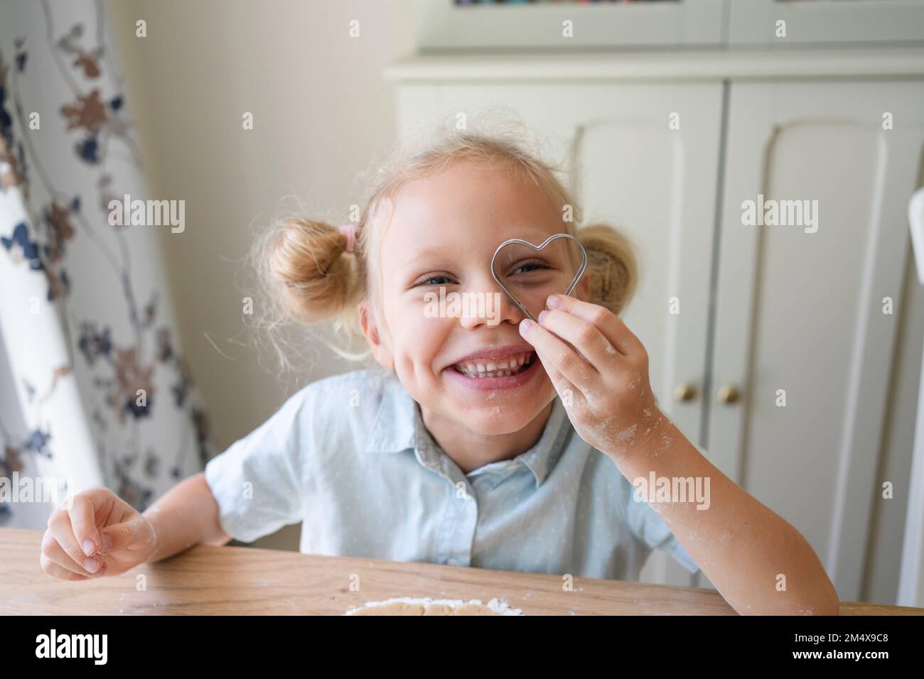 Glückliches Mädchen, das durch herzförmigen Keksschneider schaut Stockfoto