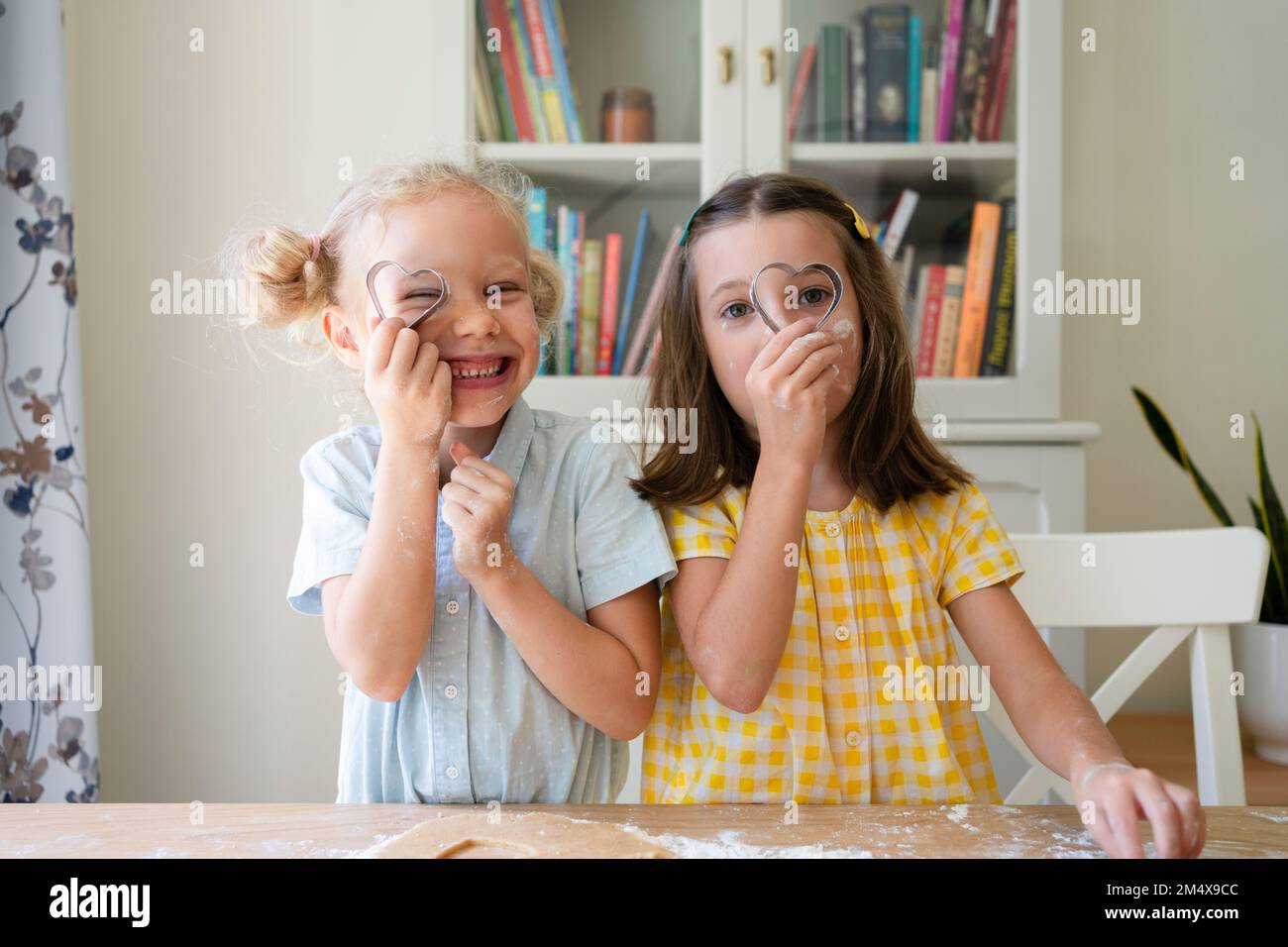 Mädchen, die zu Hause durch einen herzförmigen Keksschneider schauen Stockfoto